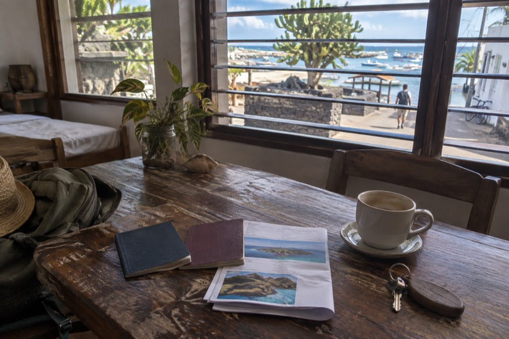 Two passports and a folded booking printout rest on a scuffed guesthouse table in Puerto Ayora, Galapagos Islands, Ecuador