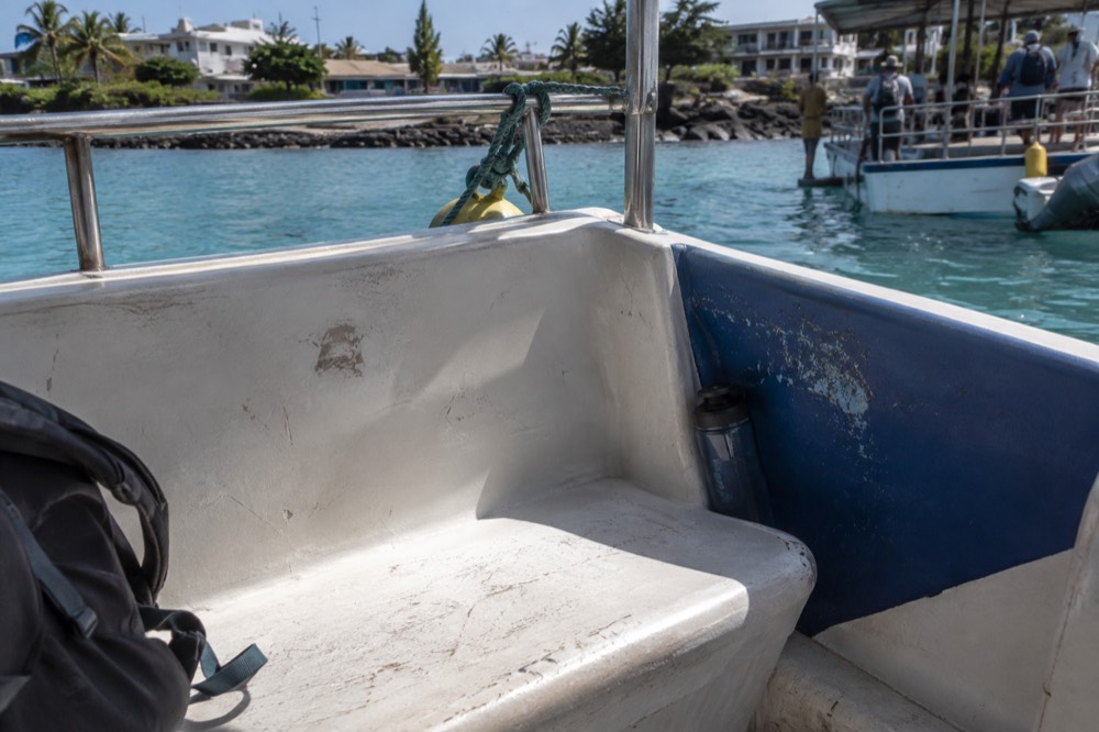 A single seat on a shared day boat moored at Puerto Ayora dock, Galapagos Islands, Ecuador, fibreglass bench scuffed and salt-stained, midday glare