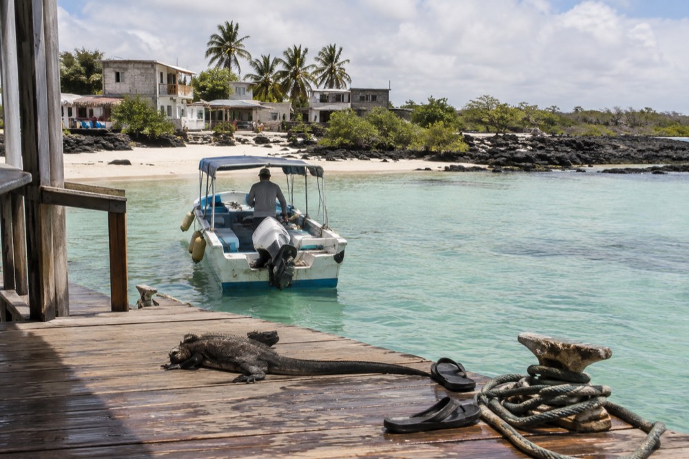 Morning in the Galapagos Islands, Ecuador: a licensed day boat idles at a sandy-floored jetty on white coral sand, turquoise shallows over it