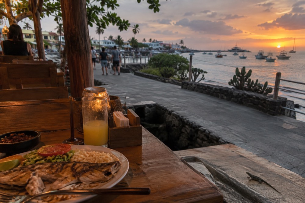 Evening in the Galapagos Islands, Ecuador: warm lamplight on a simple waterfront eatery table of scuffed local hardwood
