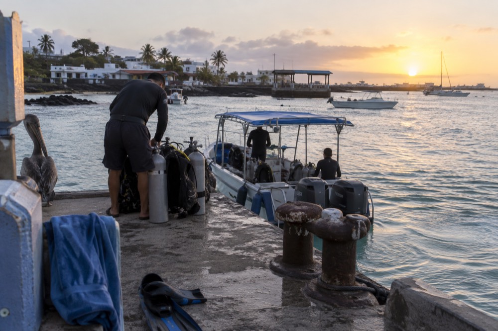 First light over a Puerto Ayora dive pier in Ecuador's Galapagos, an operator checking a tank while the day's only dive slot loads