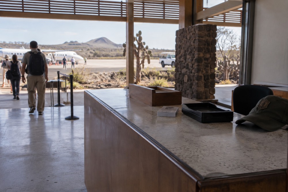Dry-season morning inside Seymour Airport on Baltra, Galapagos Islands, Ecuador: a scuffed formica ticket counter with a paper stub and coin tray