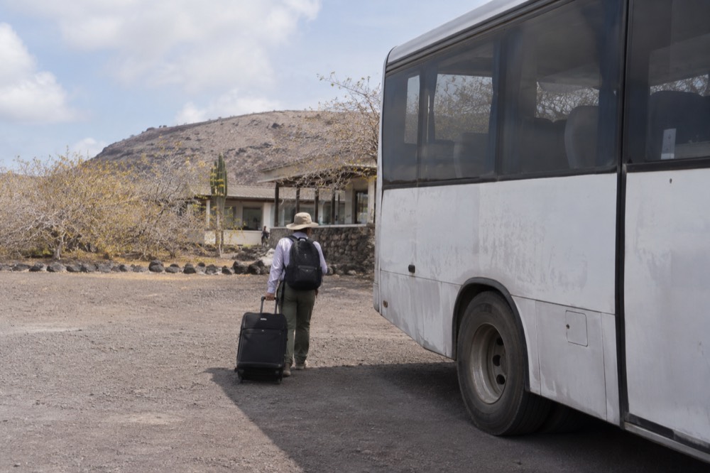 Mid-morning at Baltra, Galapagos Islands, Ecuador: an airport shuttle bus waits on dusty volcanic gravel