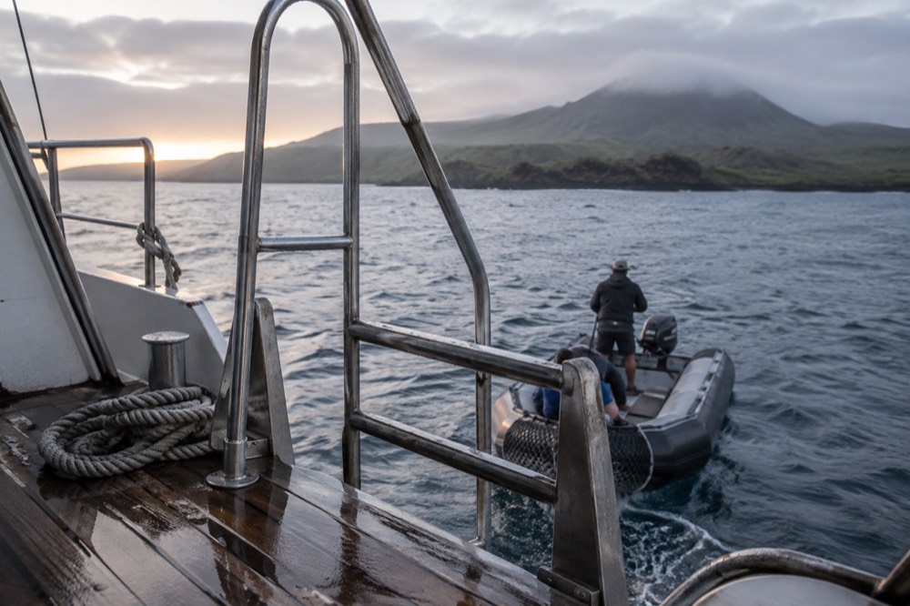 A small cruise ship's wet aft deck ladder and coiled mooring rope at dawn off Floreana Island, Galapagos Islands, Ecuador, a panga alongside
