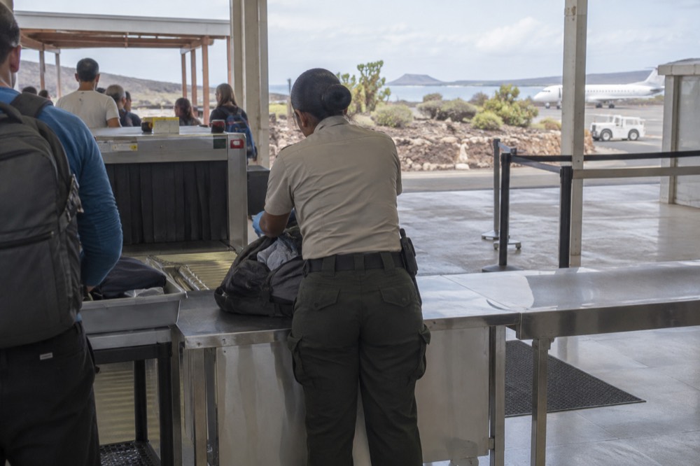 Airport inspection lane at Seymour Airport on Baltra, Galapagos Islands, Ecuador, an open duffel on the steel counter under fluorescent morning light