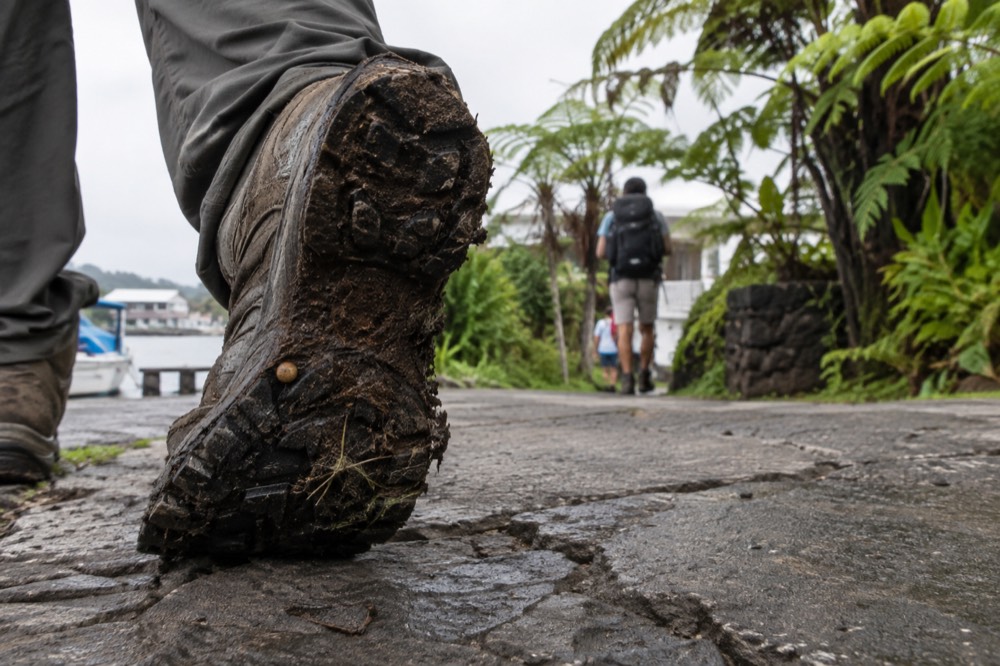 A boot tread caked with highland mud rests on cracked concrete at a trailhead near Puerto Ayora, Galapagos Islands, Ecuador, humid overcast morning