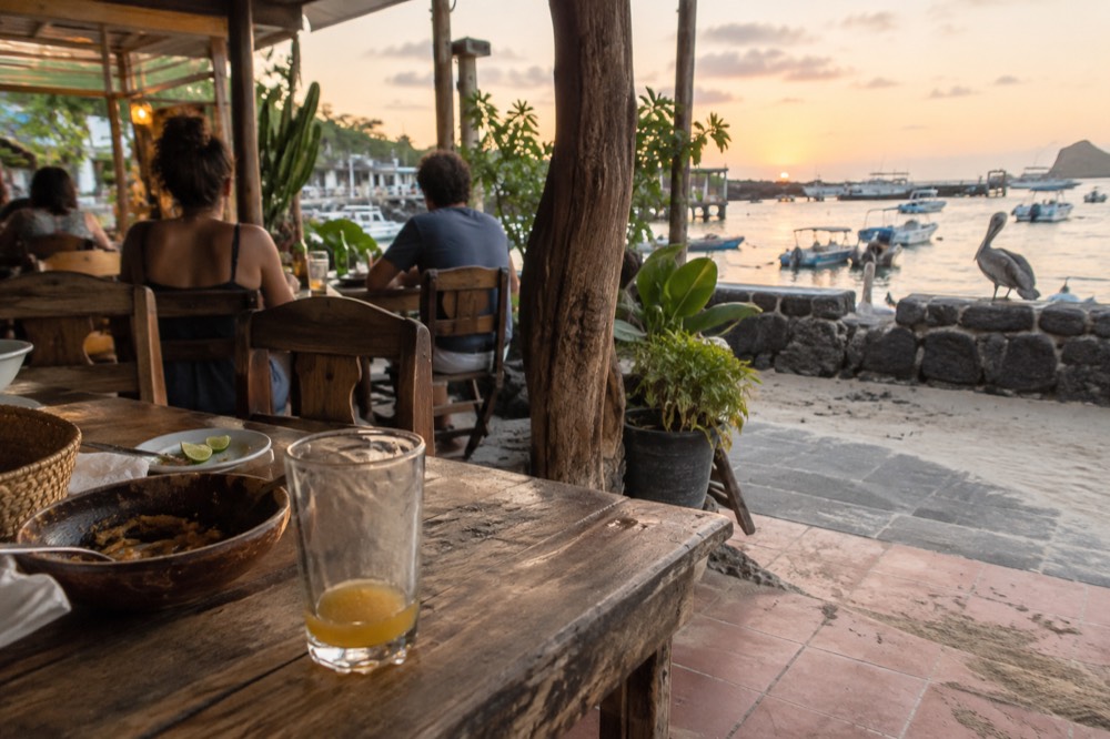 A scuffed wooden table at an open-fronted restaurant in Puerto Ayora, Galapagos Islands, Ecuador, barefoot diners blurred behind