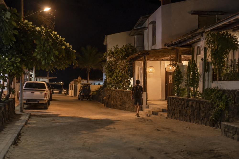 Night on a quiet sandy street in Puerto Baquerizo Moreno, Galapagos Islands, Ecuador: warm lamplight on low rendered buildings